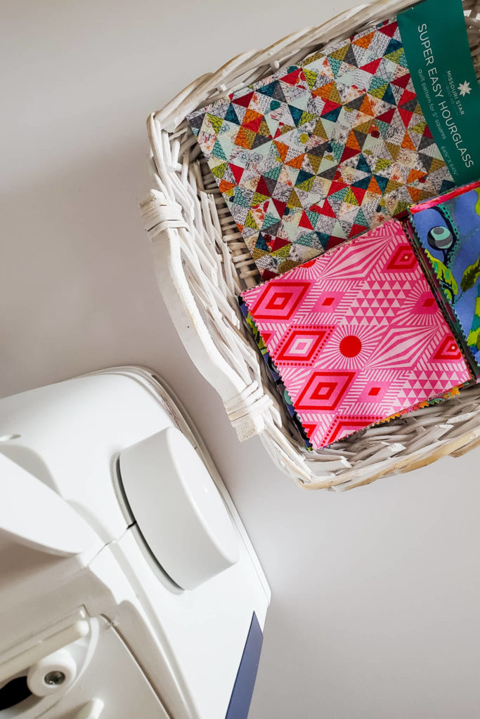 Sewing machine and wicker basket full of 5" fabric squares and a quilt pattern.