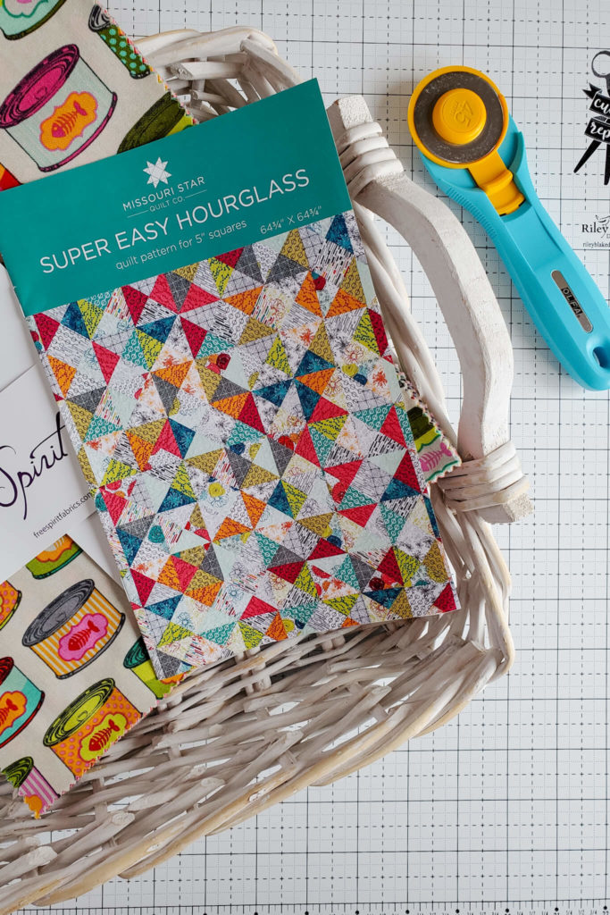 Wicker basket with a quilt pattern and layer cake. A rotary cutter lays beside the wicker basket.